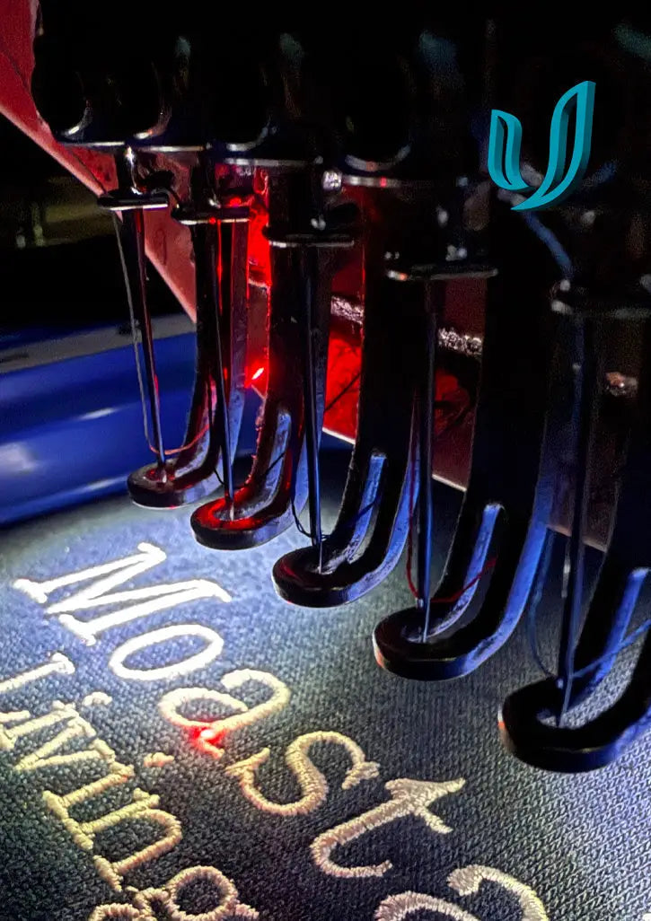 Multi-needle embroidery machine stitching text onto dark fabric with colorful embroidery threads