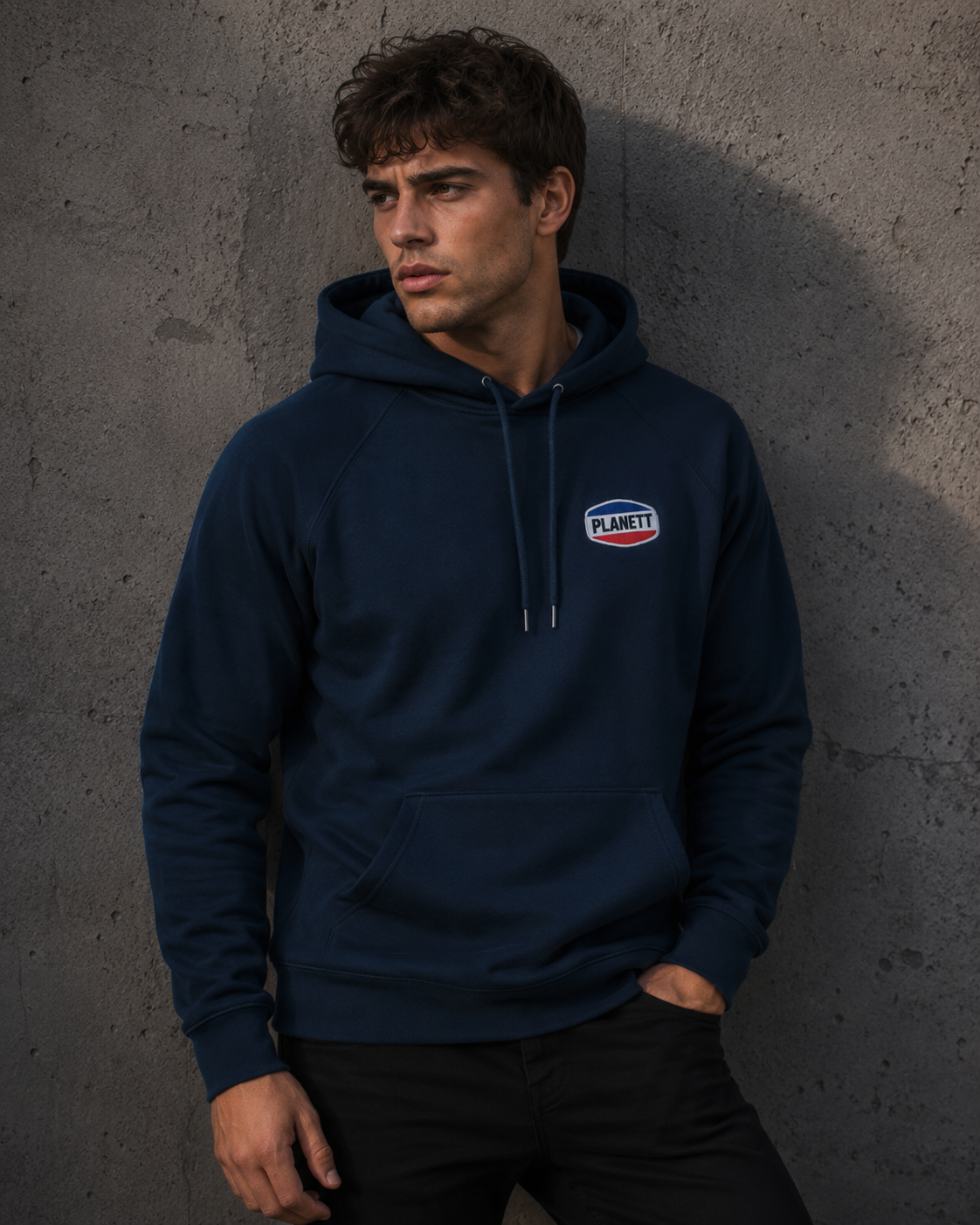 Man wearing a navy blue hoodie with a logo against a gray concrete wall