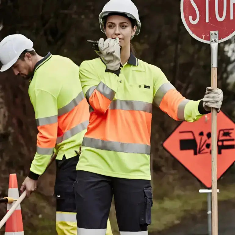 Two workers wearing high visibility safety gear in Australia with stop sign and traffic cone for roadwork and construction safety